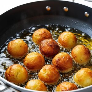 Action shot of crispy potato balls frying in a deep pan of hot oil with bubbles forming around them Action shot of crispy potato balls frying in a deep pan of hot oil with bubbles forming around them