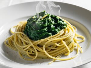 Close up of spaghetti with spinach sauce on a white plate with steam rising and a sprinkle of black pepper. makaron z kremowym sosem