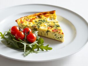Porcja na talerzu Elegancko podana porcja frittaty na bialym talerzu. Obok salatka z rukoli i pomidorkow koktajlowych
