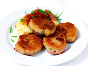 Zlociste kotlety na talerzu Swiezo usmazone kotlety mielone podane na bialym talerzu z ziemniakami puree i surowka z kapusty kiszonej. 1 1