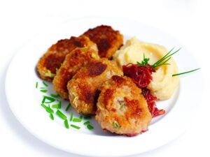 Zlociste kotlety na talerzu Swiezo usmazone kotlety mielone podane na bialym talerzu z ziemniakami puree i surowka z kapusty kiszonej.